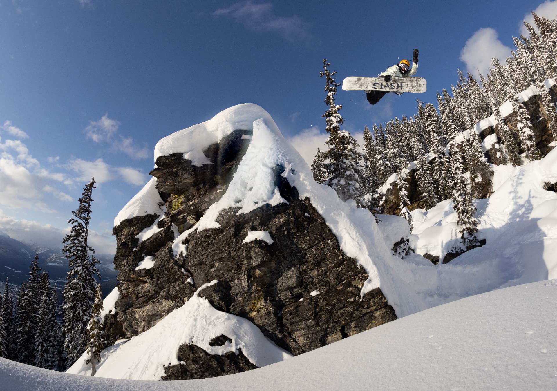 A snowboarder airborne off a snow-covered cliff band above deep powder